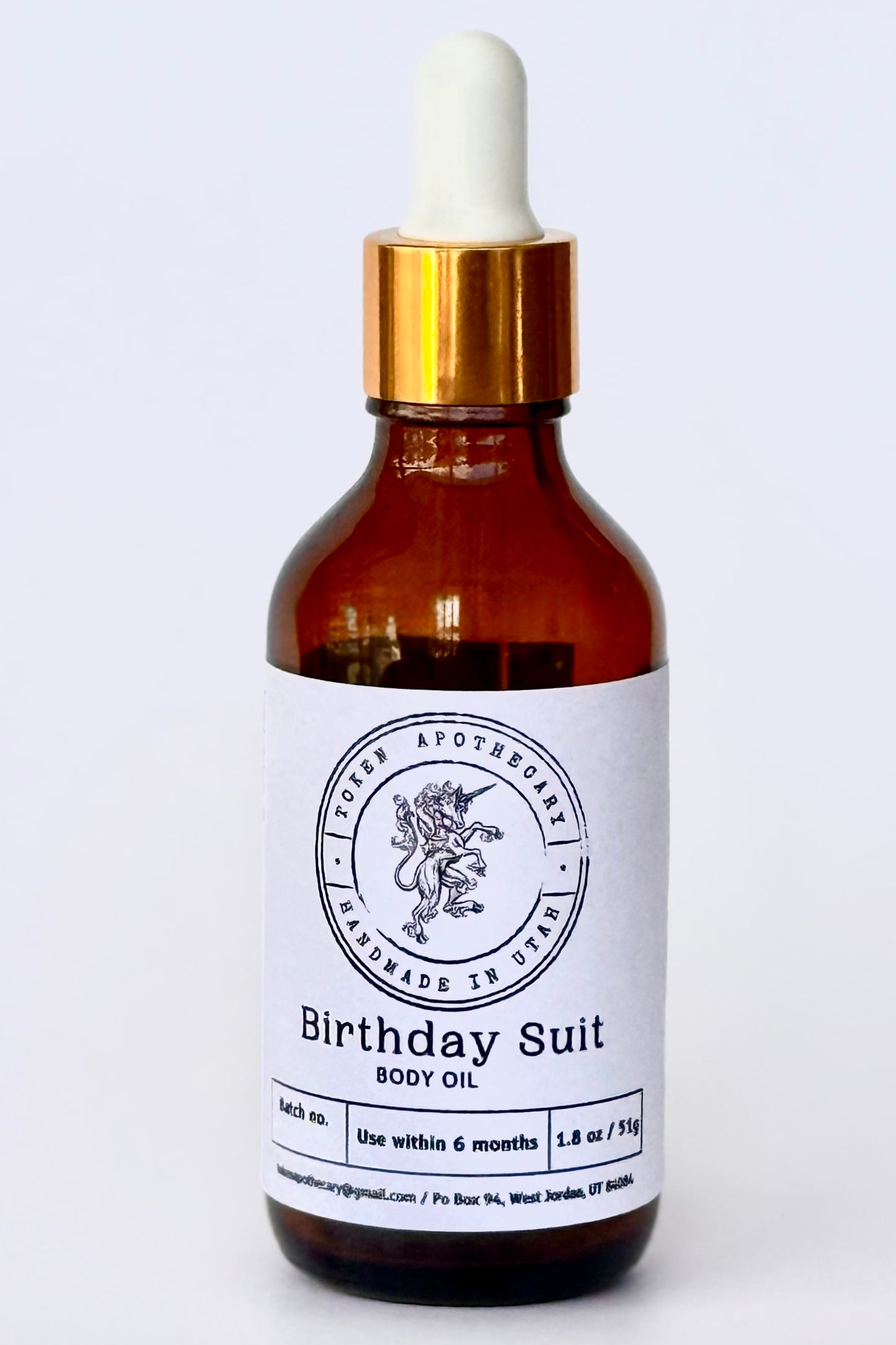Bottle of 'Birthday Suit' body oil with a dropper on a white background